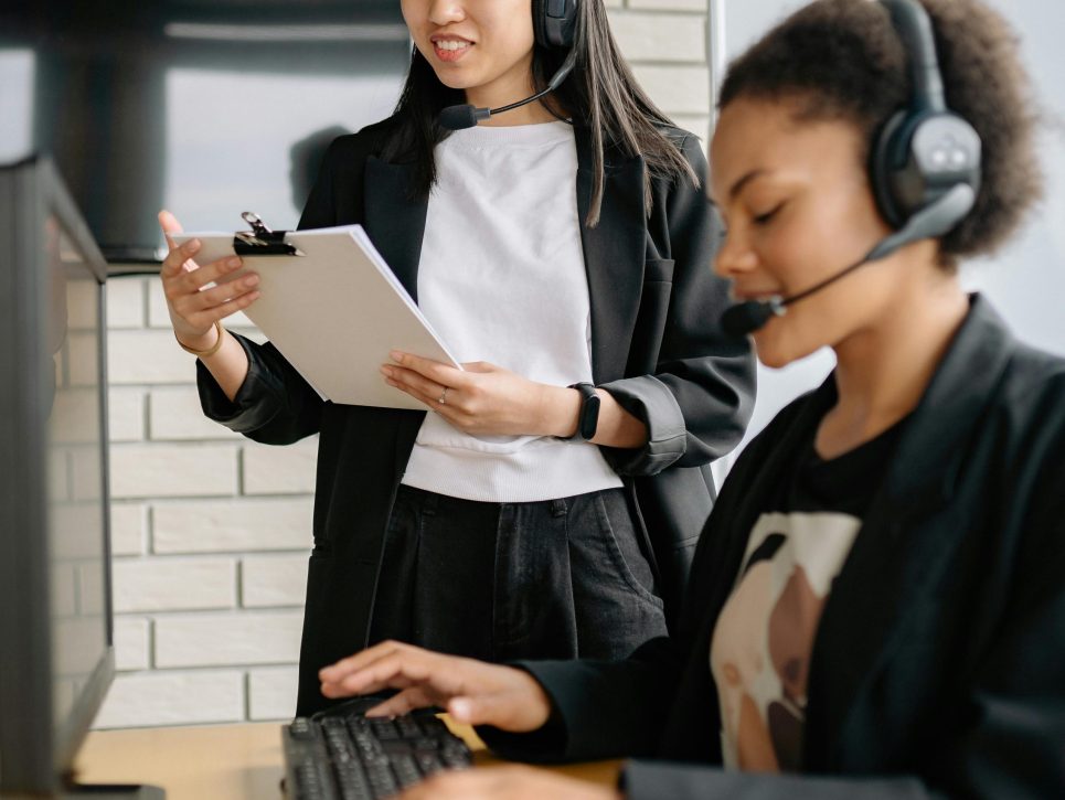 Two women in a call center working with headsets and computers, focusing on customer support.